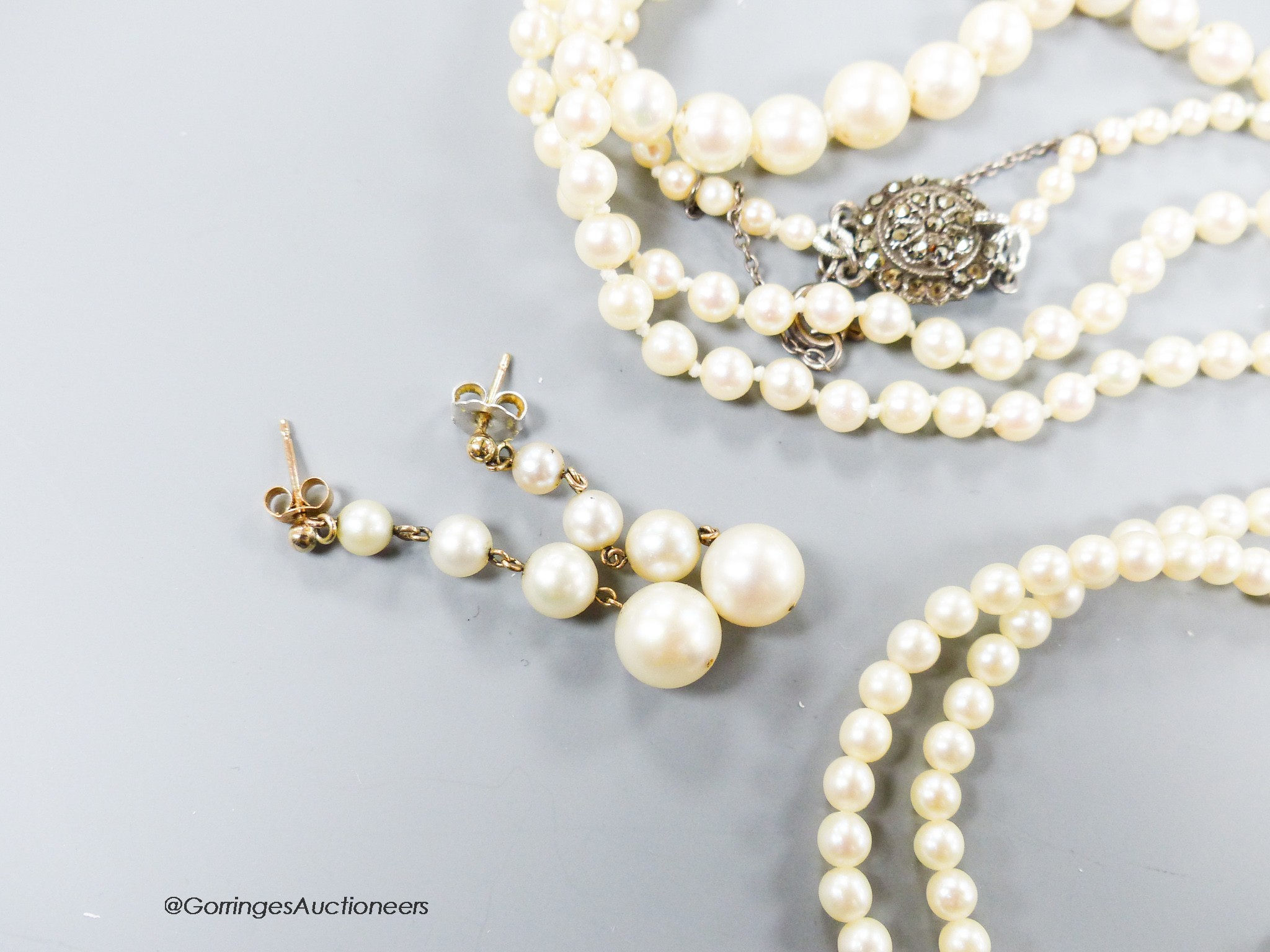 A long single strand graduated cultured pearl necklace, with marcasite clasp, 90cm, one other similar smaller necklace, a similar double strand bracelet and a pair of earrings(a.f.).